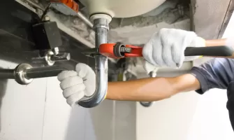 Plumber fixing white sink pipe with adjustable wrench.